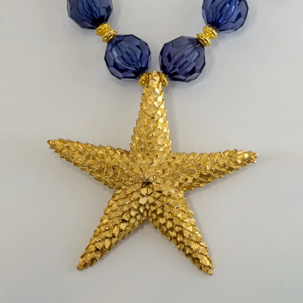 Closeup of a bold vintage statement necklace centers on a 3.25-inch, 5-point, star shaped textured gold-tone pendant.