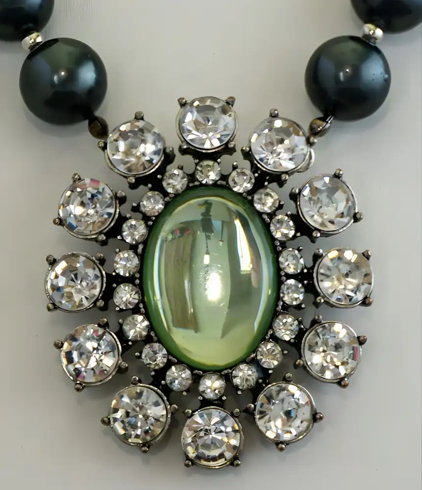 Closeup of a vintage statement necklace centers on a dramatic 2" x 2.375" oval pendant featuring a light green glass centerpiece framed by two sizes of shimmering clear rhinestones.