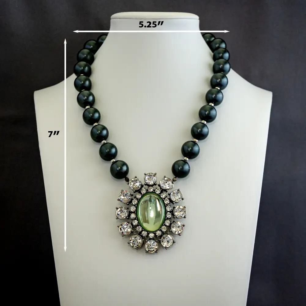 Dimensions of a vintage statement necklace centers on a dramatic 2" x 2.375" oval pendant featuring a light green glass centerpiece framed by two sizes of shimmering clear rhinestones.
