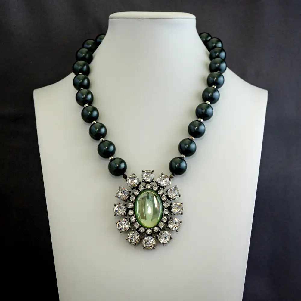 vintage statement necklace centers on a dramatic 2" x 2.375" oval pendant featuring a light green glass centerpiece framed by two sizes of shimmering clear rhinestones.