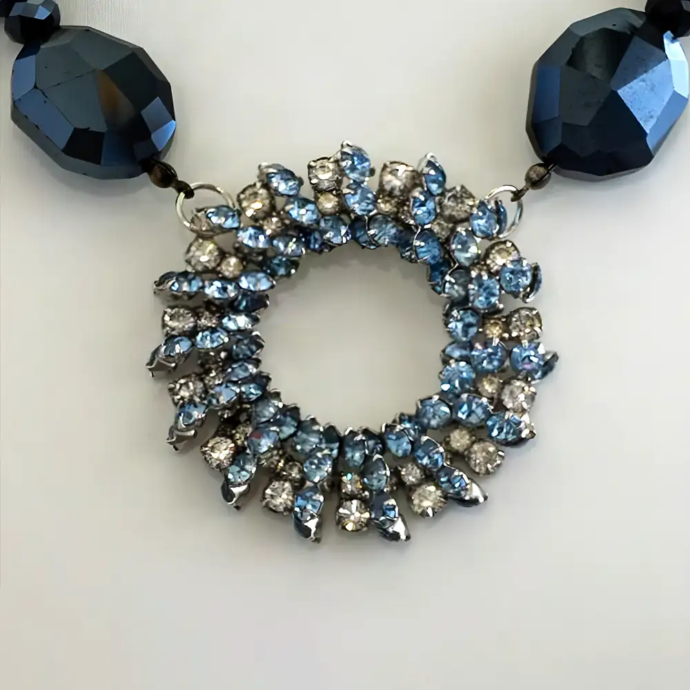 Close up of an elegant necklace features a vintage 2-inch circular pendant filled with a sparkling mix of pale blue and clear rhinestones.