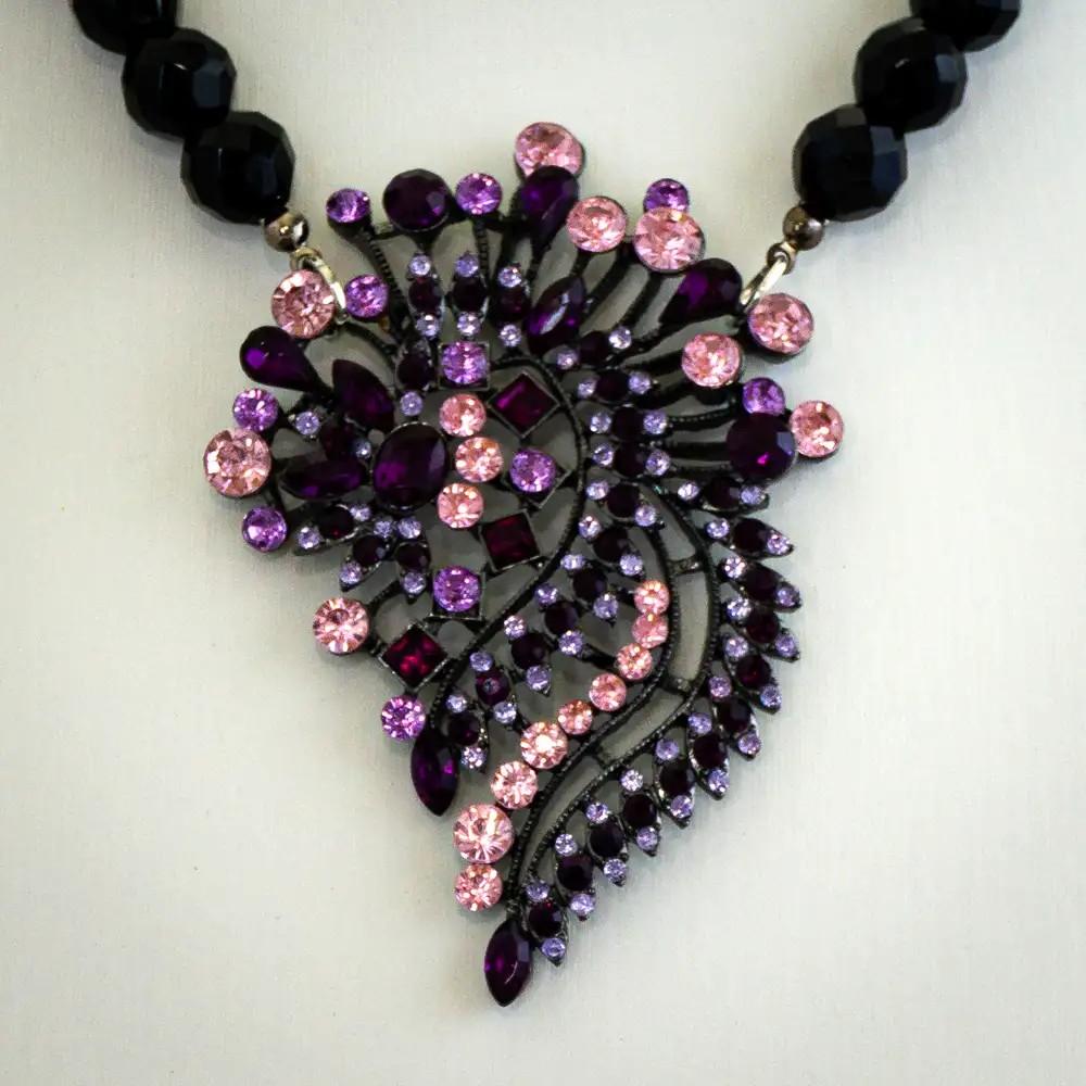 Closeup of a vintage necklace features a dramatic 2.25" by 3.25" pendant, brilliantly adorned with bright pink, dark purple, and lavender rhinestones.