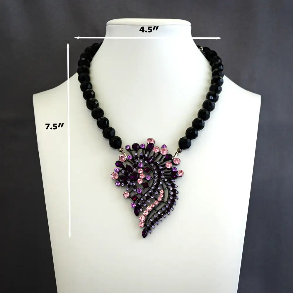 Dimensions of a vintage necklace features a dramatic 2.25" by 3.25" pendant, brilliantly adorned with bright pink, dark purple, and lavender rhinestones.