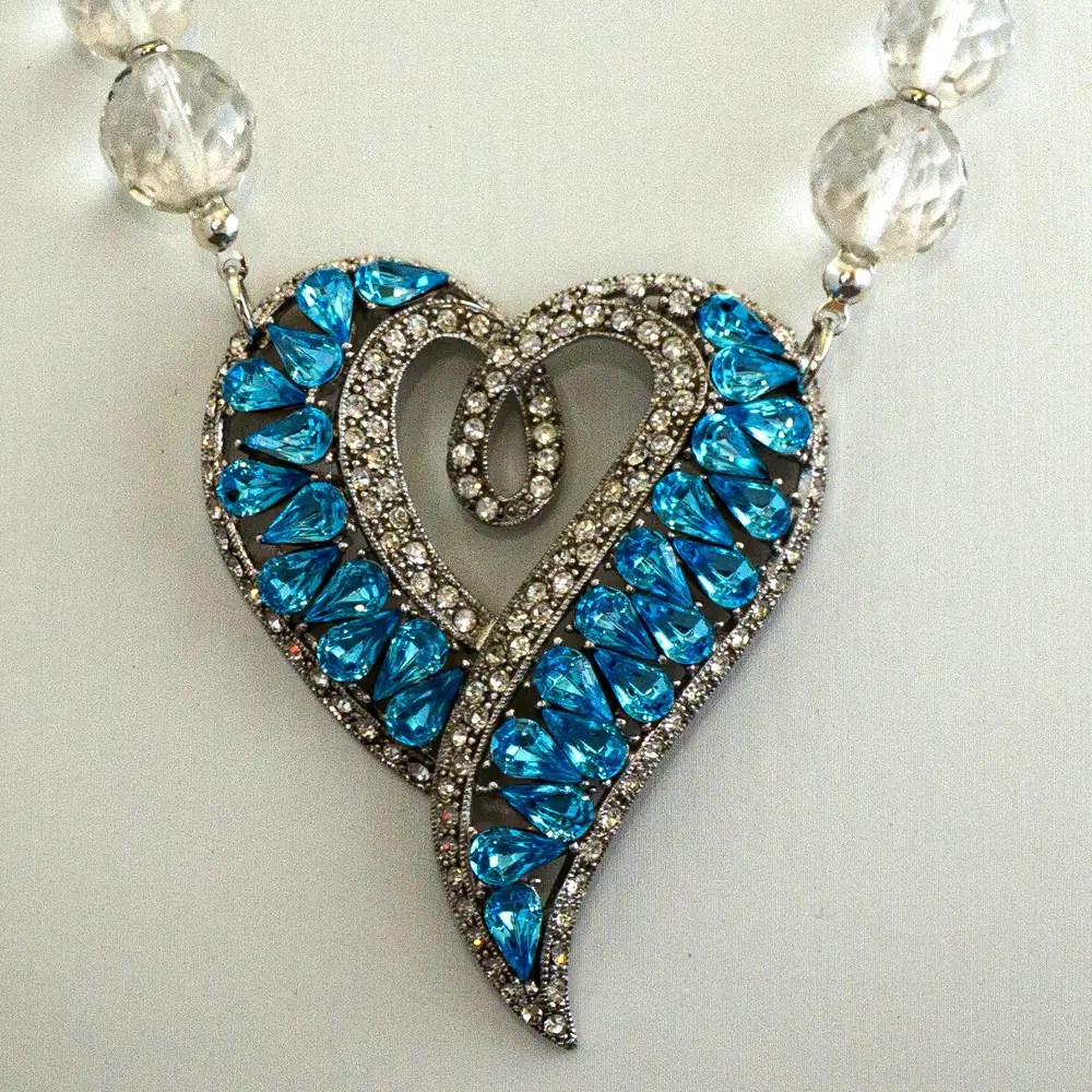 Close up of this statement necklace centers on a stylized heart pendant (2′′ wide×2.5′′ long) featuring vibrant turquoise framed by brilliant clear rhinestones.