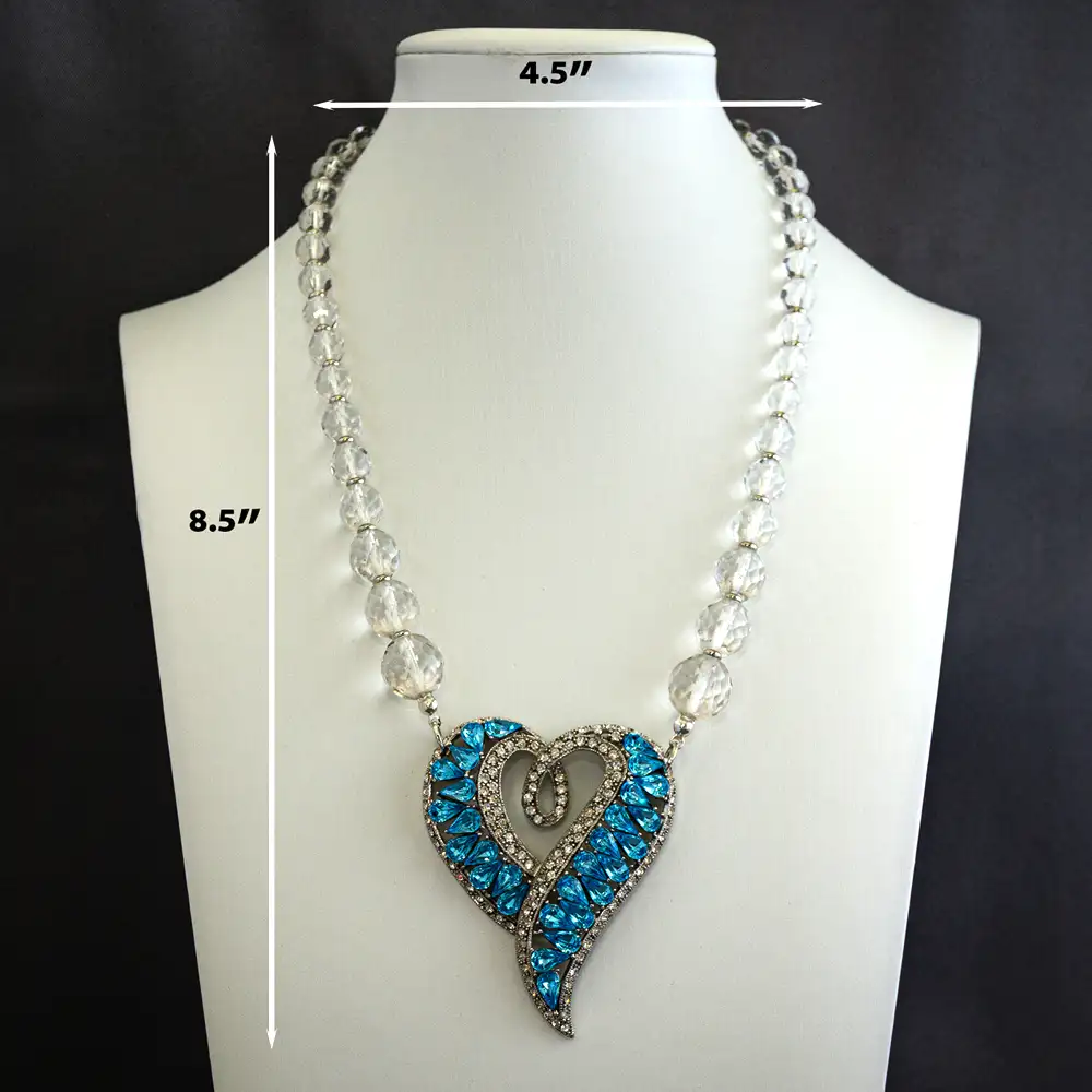 Description of this statement necklace centers on a stylized heart pendant (2′′ wide×2.5′′ long) featuring vibrant turquoise framed by brilliant clear rhinestones.