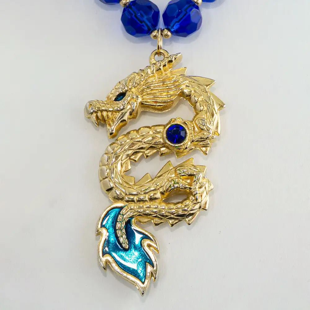 close up of A striking vintage gold-tone dragon pendant takes center stage, detailed with a brilliant cobalt blue rhinestone and enamel inlays in deep cobalt and vibrant teal.