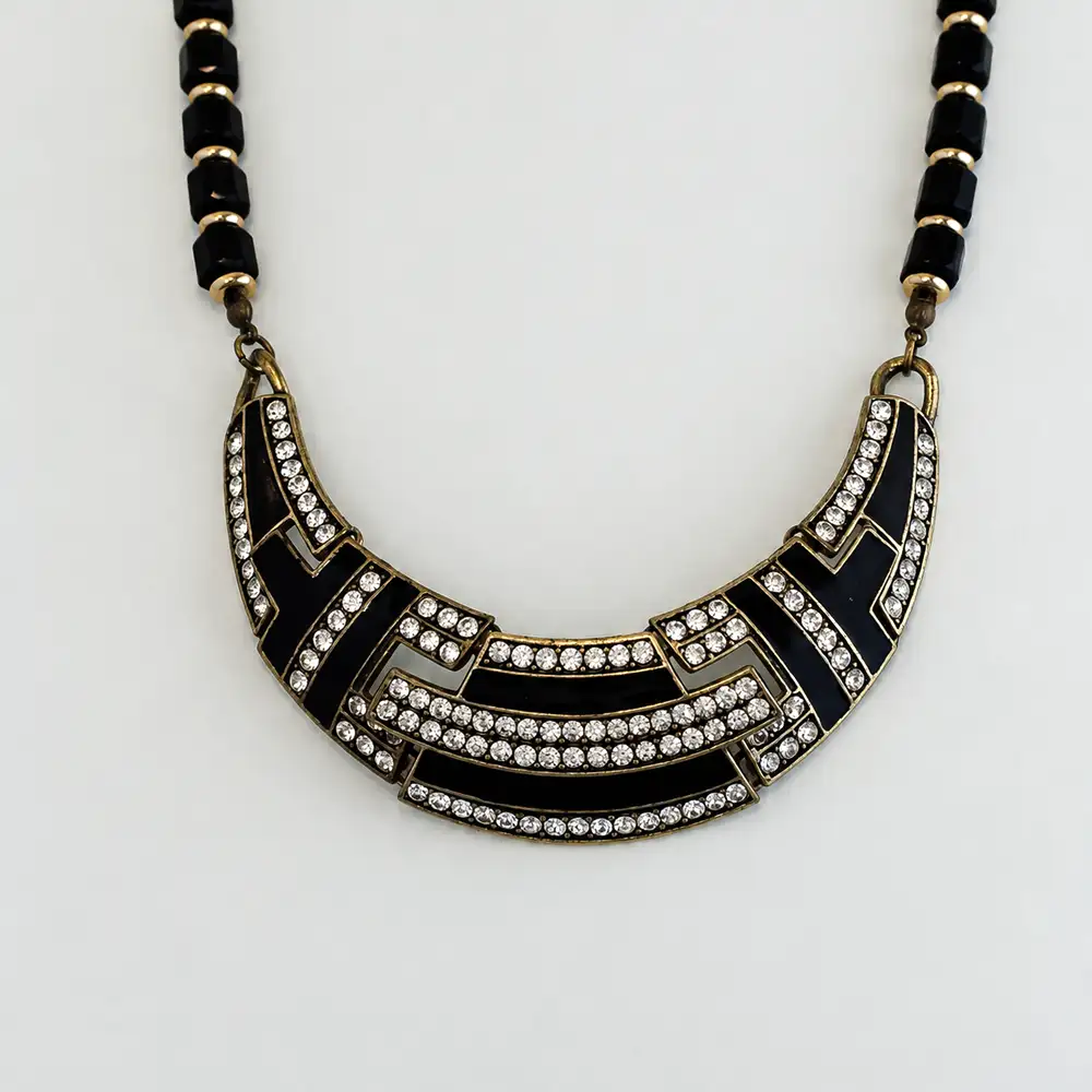 Close up of vintage-inspired 16-inch necklace features a striking Art Deco bib pendant adorned with sleek black enamel and sparkling clear rhinestones set in rich, antiqued gold