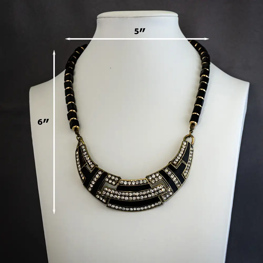 Dimension of Close up of vintage-inspired 16-inch necklace features a striking Art Deco bib pendant adorned with sleek black enamel and sparkling clear rhinestones set in rich, antiqued gold