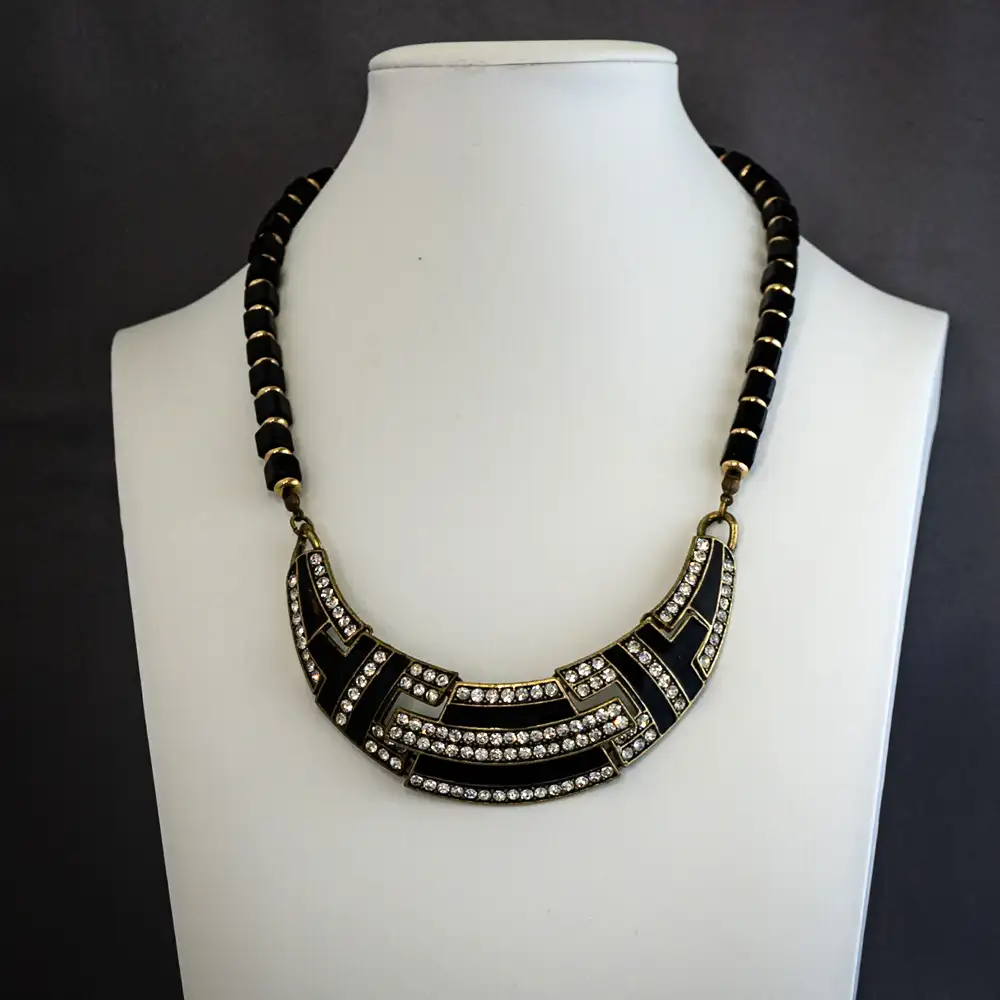 vintage-inspired 16-inch necklace features a striking Art Deco bib pendant adorned with sleek black enamel and sparkling clear rhinestones set in rich, antiqued gold