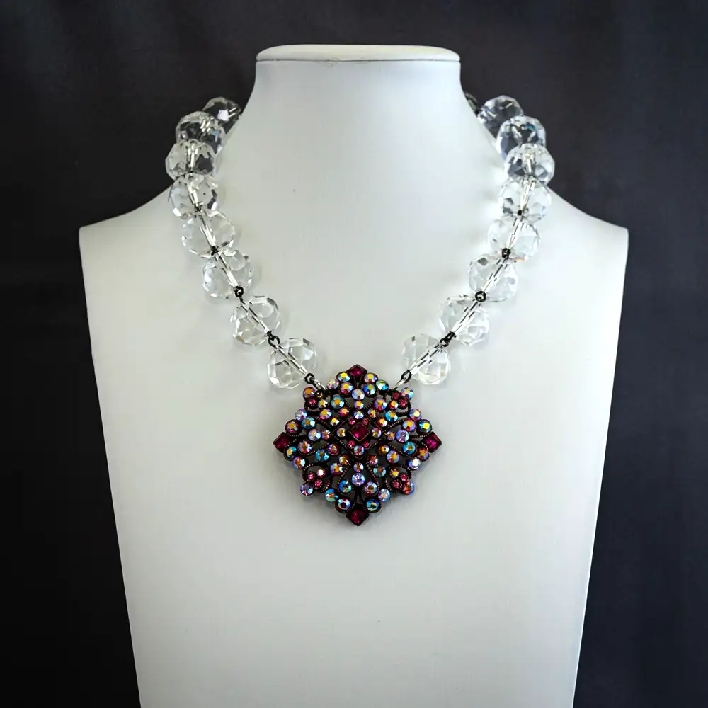 This vintage 15.5-inch necklace features a signed Joan Rivers filigree pendant set with mesmerizing pink and purple aurora borealis rhinestones that catch the light with brilliant color.