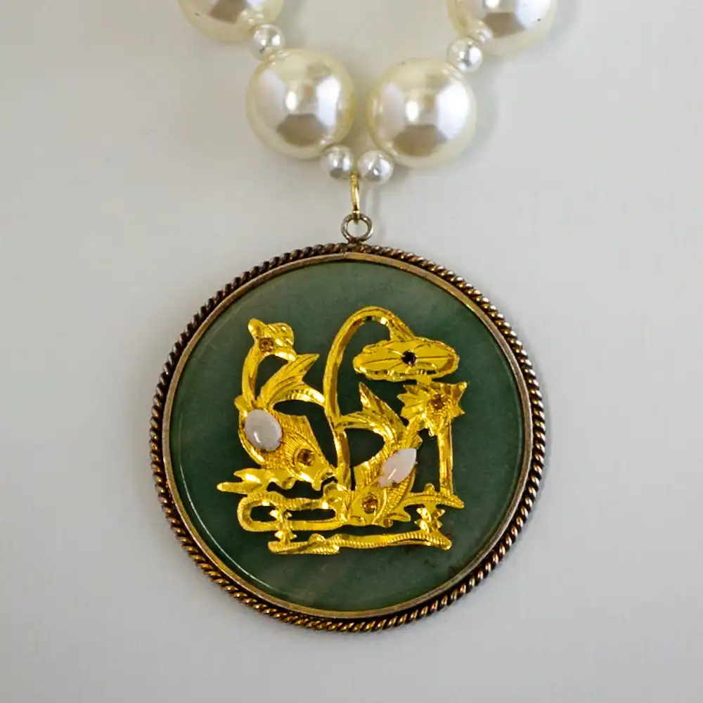 Closeup of a vintage statement necklace centers on a remarkable 2.5" light green jade medallion, featuring a gold-tone applique set with two small opals and five sparkling rhinestones.