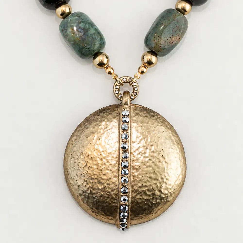 close up of a striking statement necklace features an eclectic strand of variegated green, amber, clear, and speckled glass beads separated by gold-tone spacers.