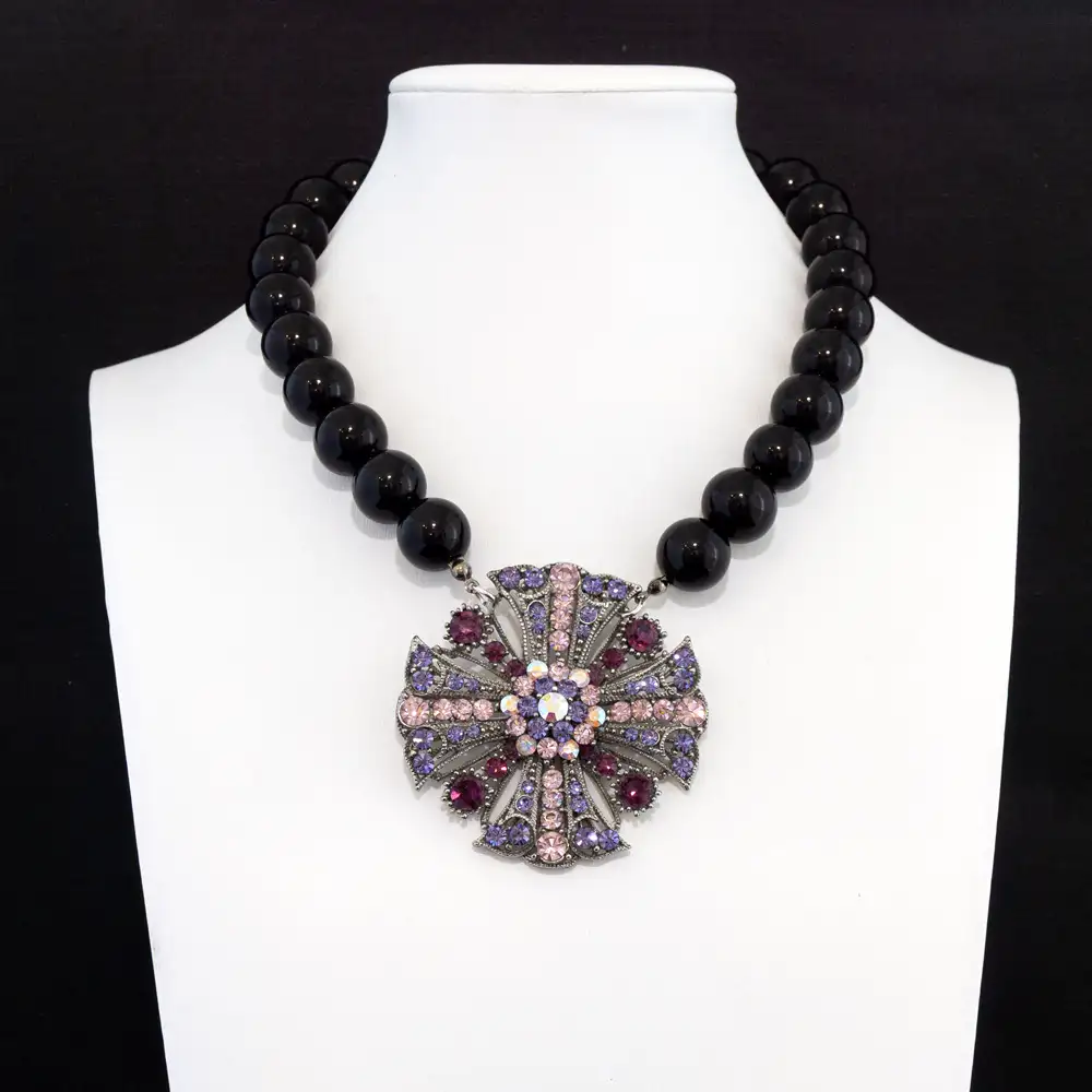 statement necklace features a strand of smooth, high-gloss black beads that beautifully frame an ornate, filigree-style metal pendant