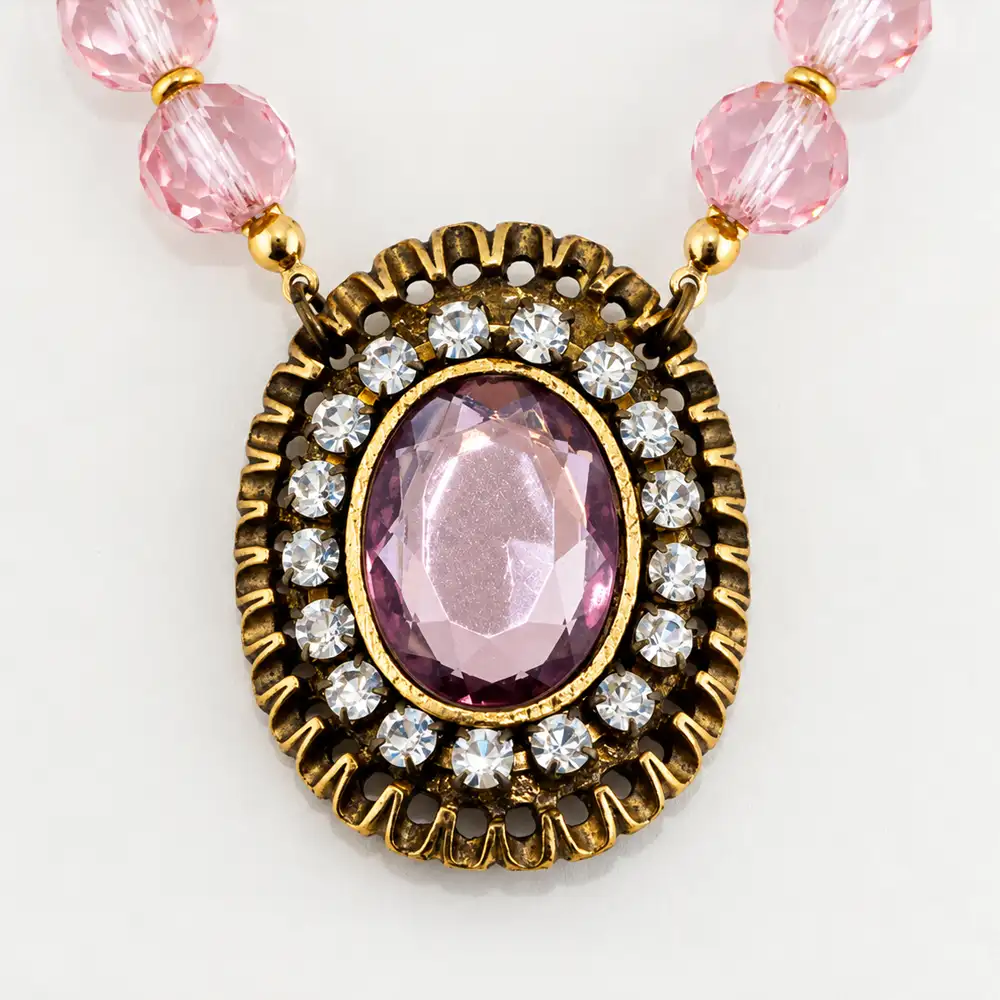 Close up of a romantic statement necklace features a strand of faceted light pink glass beads that reflect a soft, luminous sparkle.