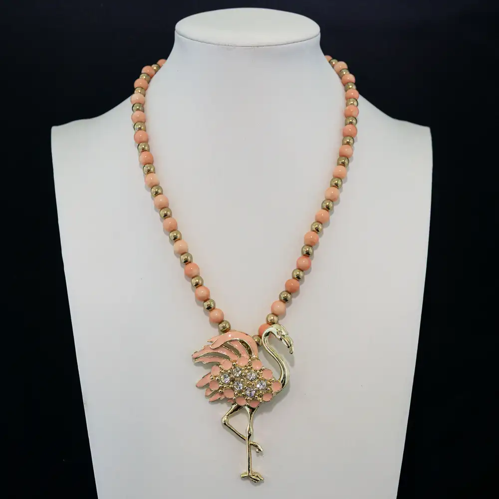 This playful necklace features soft peach coral round beads strung with polished gold-tone accent beads.