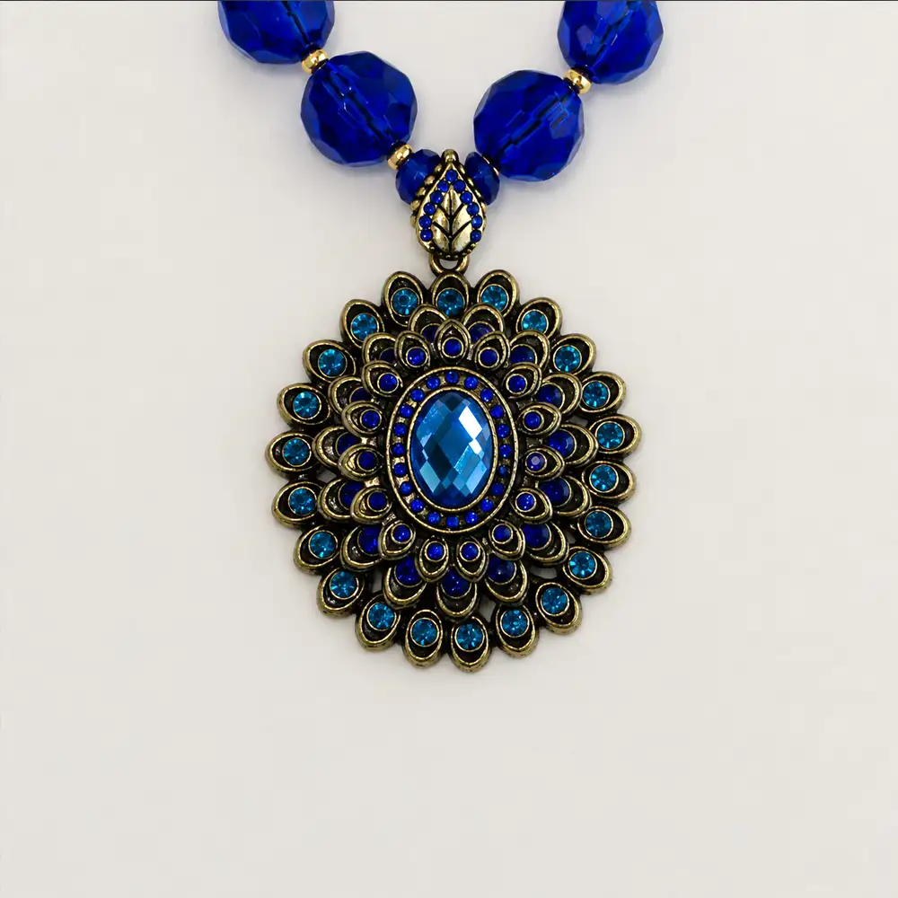 Closeup of a 2-inch round vintage pendant, this 16-inch necklace features radiant cobalt and teal rhinestones nestled in antiqued gold settings.
