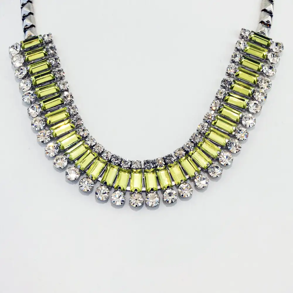 Closeup of a dazzling vintage statement necklace features a striking band of baguette-cut, peridot-green rhinestones set in a silver-tone frame.
