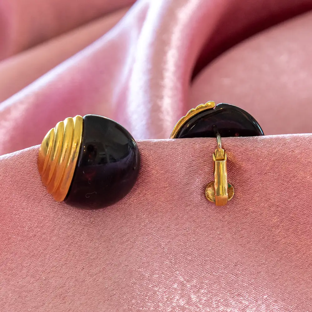 bold vintage clip-on earrings feature smooth, black dome cabochons elegantly paired with ribbed, fan-like gold-toned metal accents