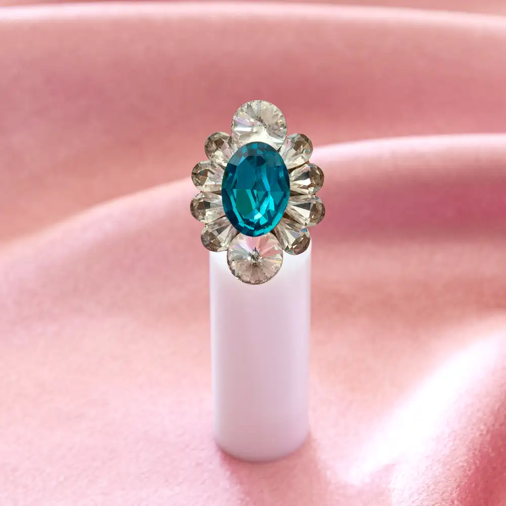 striking cocktail ring features a vibrant oval teal stone encircled by clear crystals on a broad, burnished silver-toned band