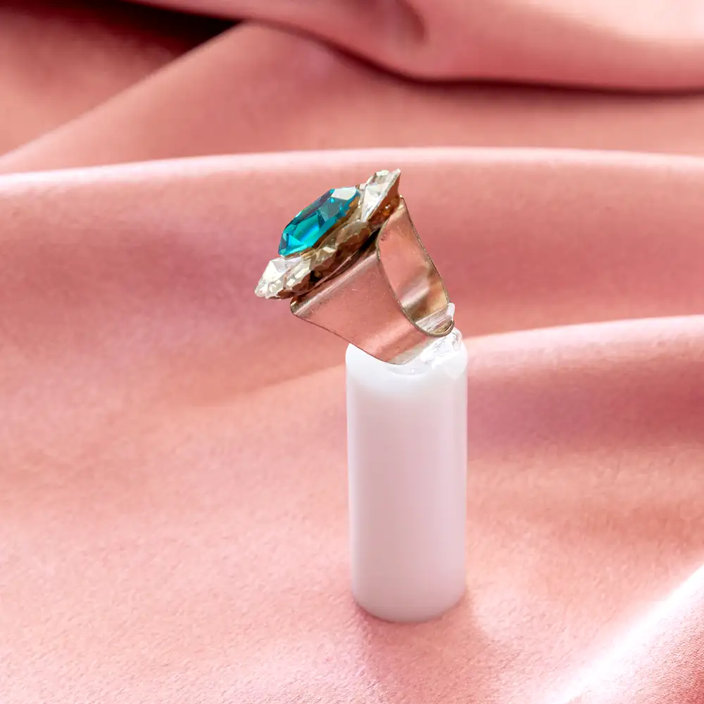 striking cocktail ring features a vibrant oval teal stone encircled by clear crystals on a broad, burnished silver-toned band